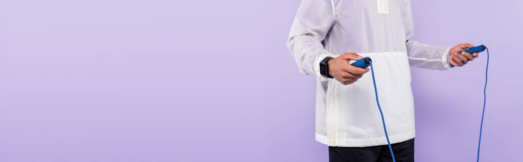 обрізаний вид афроамериканця в модному спортивному одязі, що тримає пропускаючу мотузку ізольовано на фіолетовому, банер
 - Фото, зображення