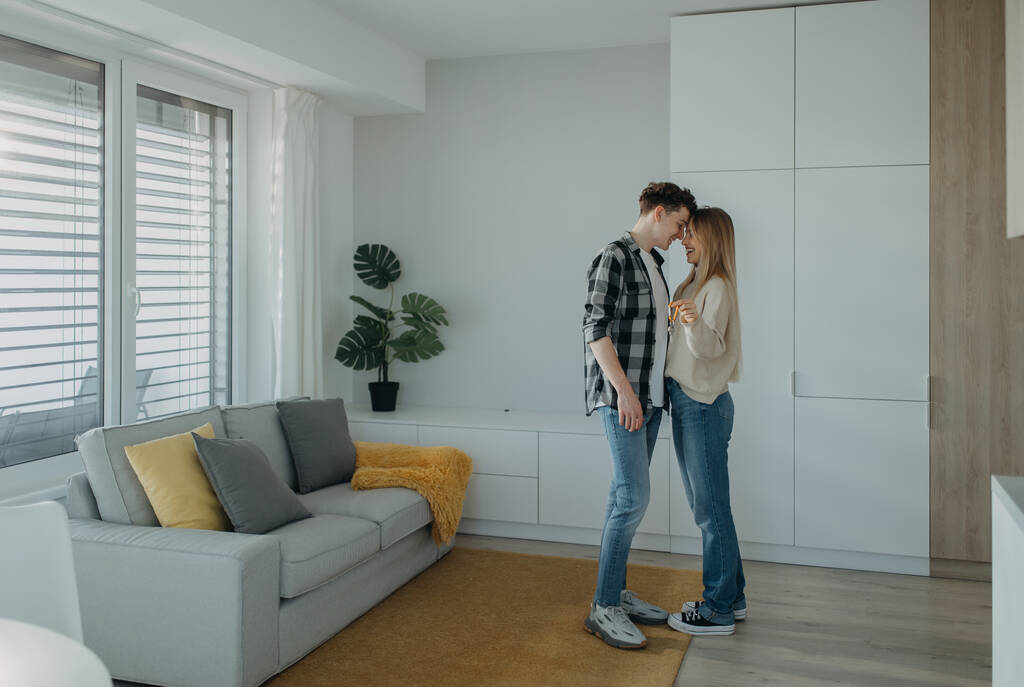 Wesoła młoda para w swoim nowym mieszkaniu, stojąca i trzymająca klucze. Pojęcie ruchu. - Zdjęcie, obraz