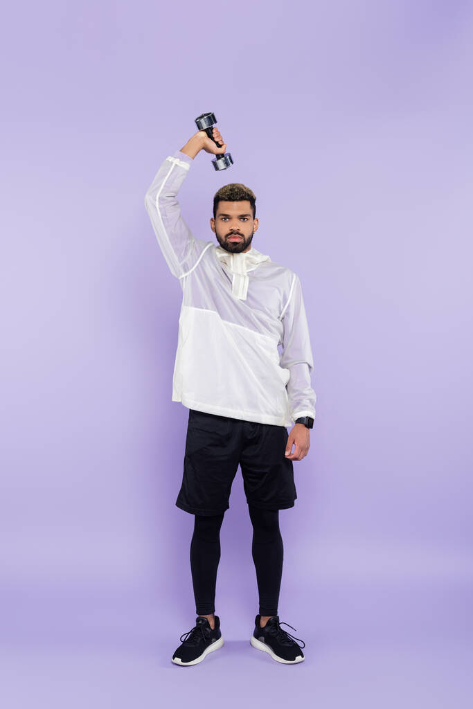 full length of bearded african american man exercising with dumbbell on purple  - Photo, Image