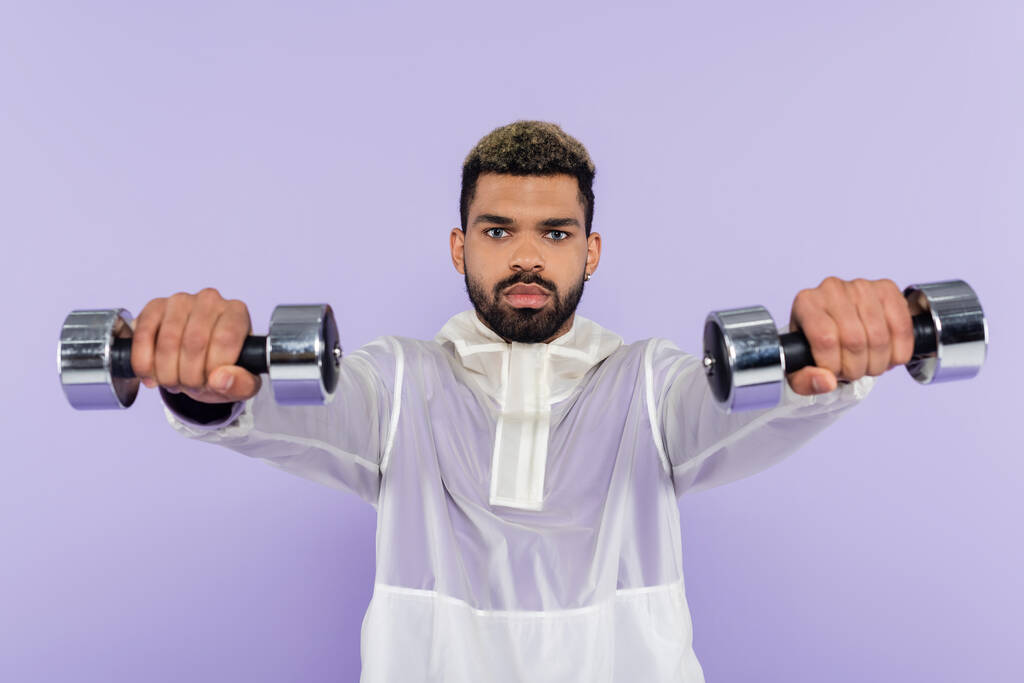 barbudo hombre afroamericano haciendo ejercicio con mancuernas aisladas en púrpura  - Foto, Imagen