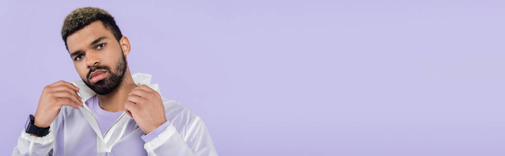 mladý africký americký sportovec s chytrými hodinkami upravující límec izolovaný na fialové, banner - Fotografie, Obrázek