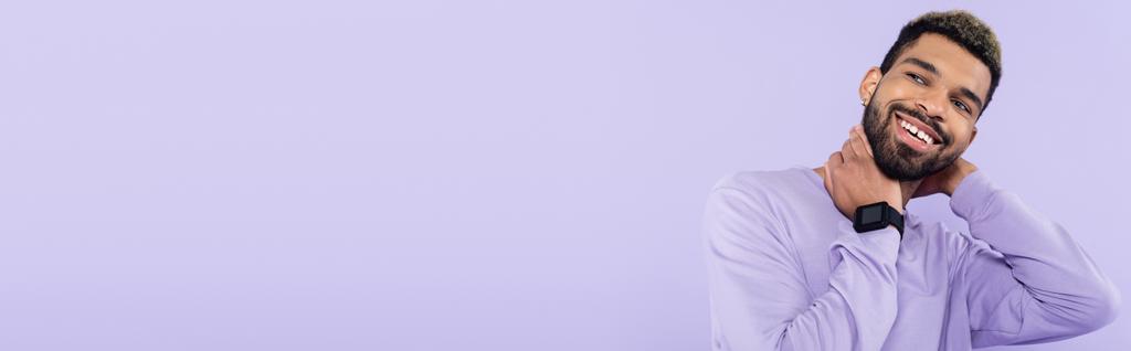 barbudo hombre afroamericano en suéter sonriendo aislado en púrpura, pancarta - Foto, imagen