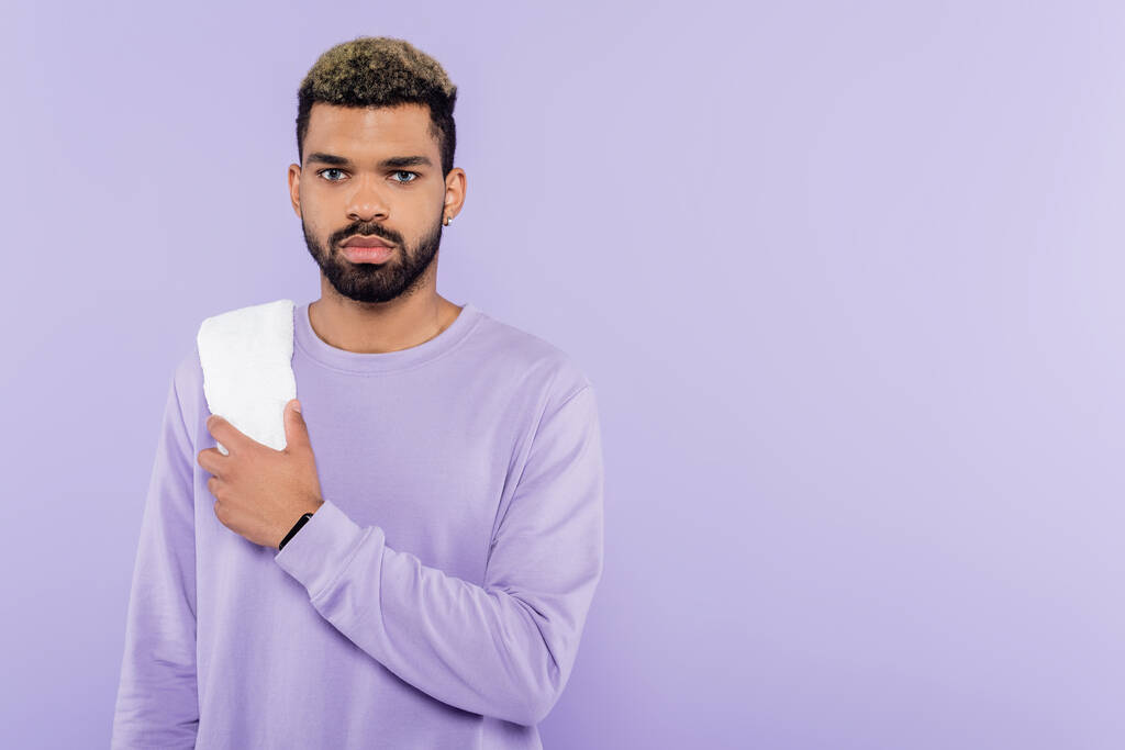 紫色に隔離された白いタオルを持ったセーターに身を包んだアフリカ系アメリカ人男性  - 写真・画像