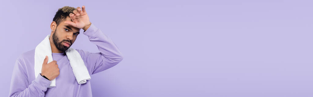 hombre afroamericano cansado en suéter sosteniendo toalla blanca y limpiando el sudor con la mano aislada en púrpura, pancarta - Foto, imagen