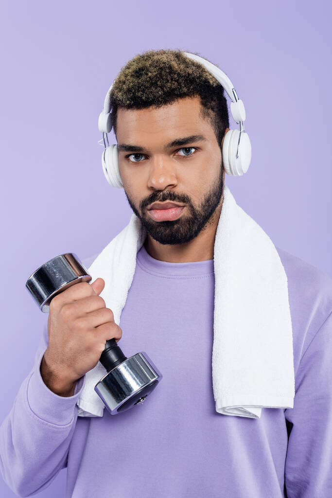barbudo hombre afroamericano en auriculares ejercitándose con mancuerna aislada en púrpura  - Foto, imagen