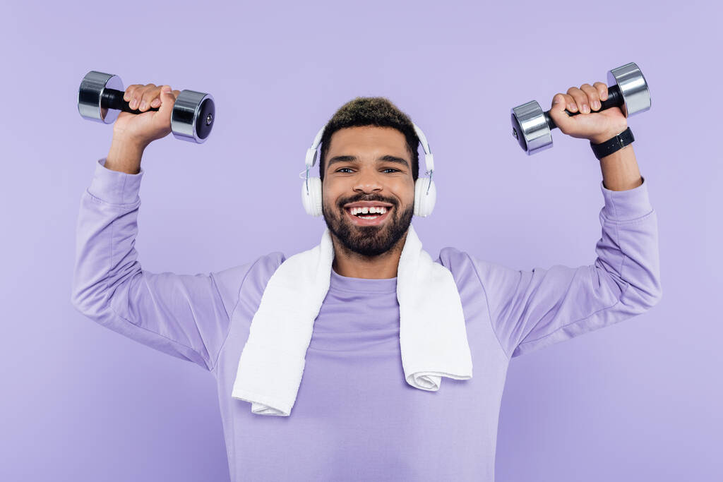 šťastný africký Američan ve sluchátkách cvičení s činky izolované na fialové  - Fotografie, Obrázek