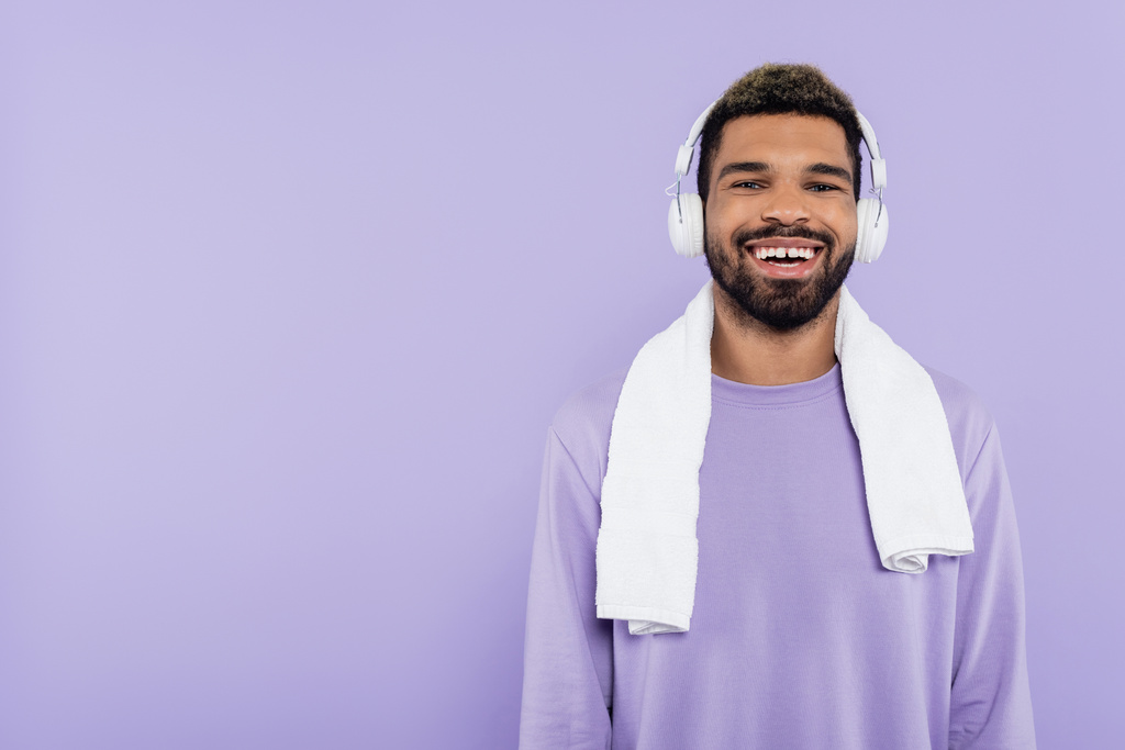 vousatý a šťastný africký Američan v bezdrátových sluchátkách izolovaných na fialové  - Fotografie, Obrázek