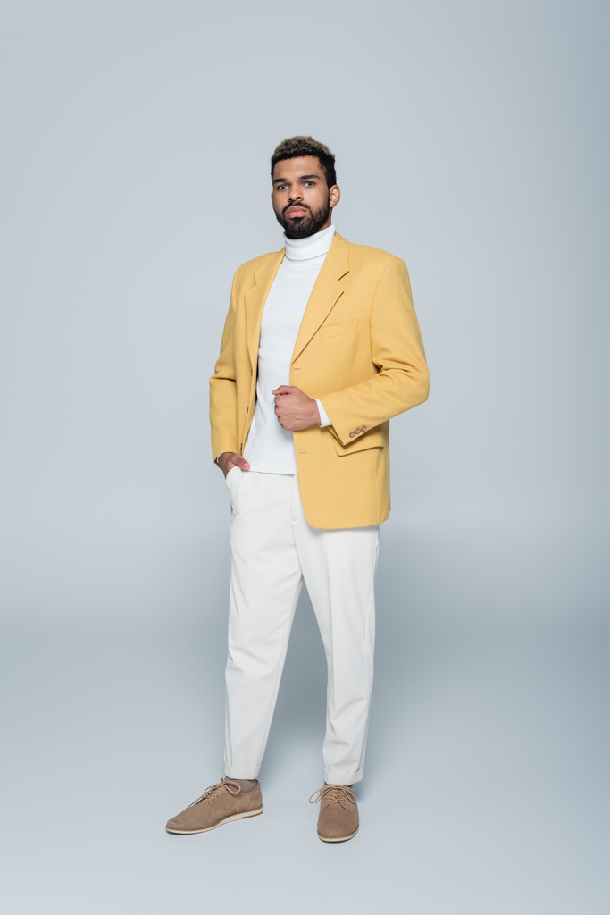 longitud completa de hombre afroamericano con estilo en chaqueta amarilla posando en gris  - Foto, Imagen