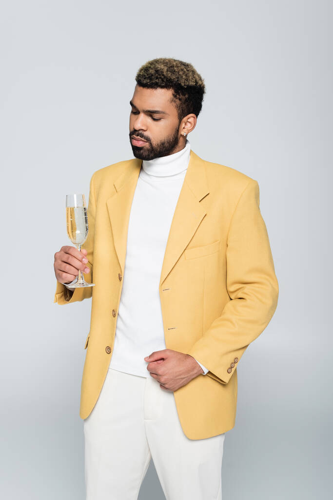 bearded african american man in stylish outfit holding glass of champagne isolated on grey  - Photo, Image