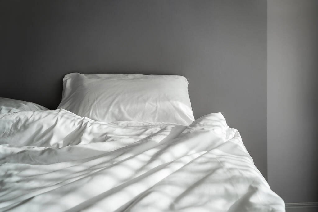 De dekens op de verfrommelde matras in de lege donkere slaapkamer - Foto, afbeelding