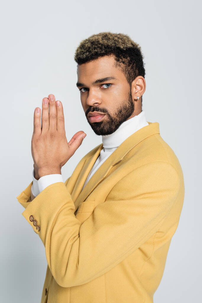 young african american man in pastel yellow blazer with praying hands isolated on grey  - Photo, Image