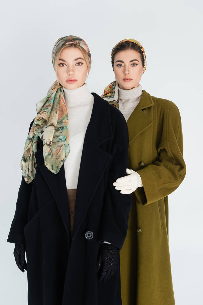 mulheres elegantes em lenços de cabeça e casacos olhando para a câmera isolada em cinza - Foto, Imagem
