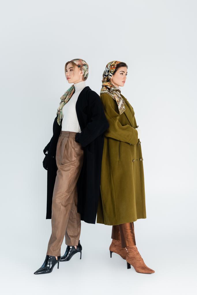 πλήρες μήκος της μόδας γυναίκες σε παλτά και μαντήλια σε γκρι φόντο - Φωτογραφία, εικόνα