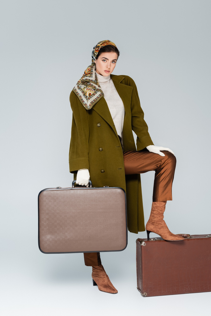 緑のコートで流行の女性の完全な長さとスカーフポーズでレトロスーツケースでグレー - 写真・画像