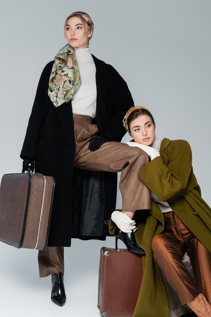 elegáns nő ölelés láb barát áll vintage bőrönd szürke háttér - Fotó, kép