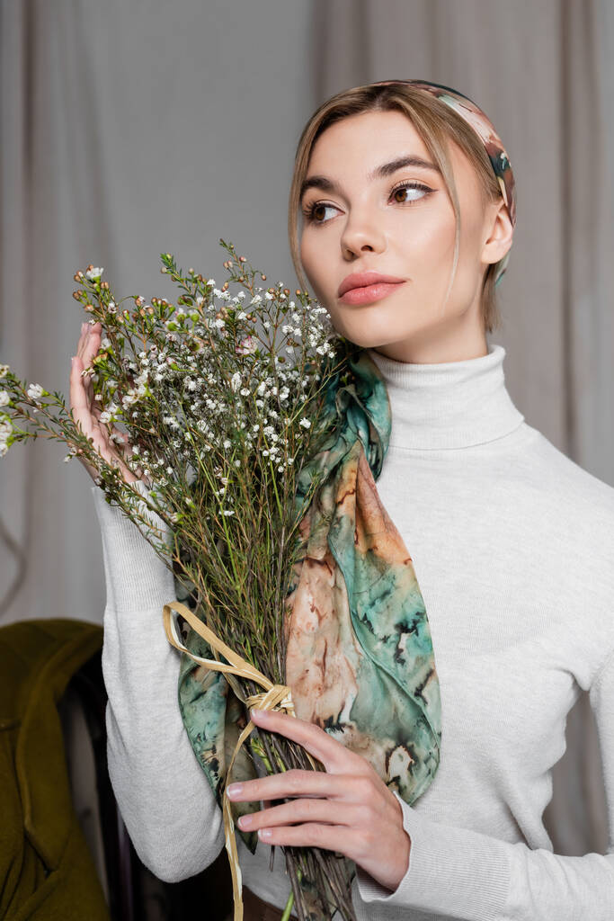 pretty woman in kerchief holding bouquet of gypsophila flowers on grey background - Photo, Image