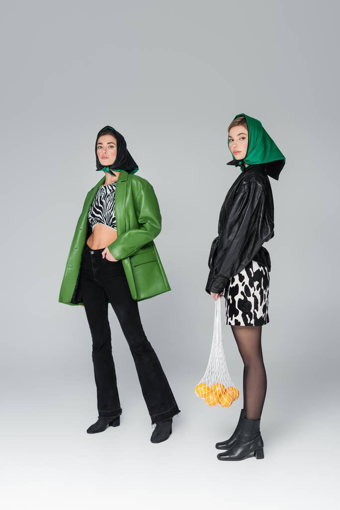 Полная длина женщины, стоящей с апельсинами в сумке рядом с модным другом на сером фоне - Фото, изображение