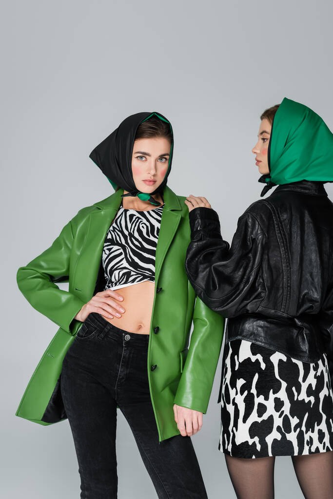 donna alla moda in giacca di pelle verde e stampa animalier in posa vicino amico isolato sul grigio - Foto, immagini
