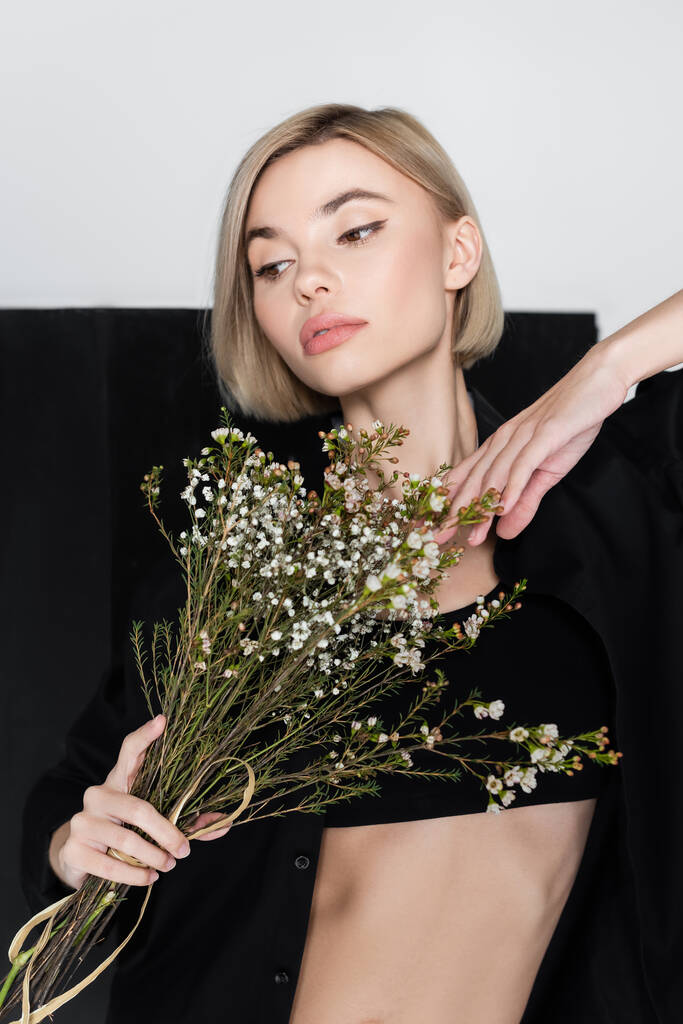 młoda blondynka pozowanie z bukietem cygańskich kwiatów na czarno-szarym tle - Zdjęcie, obraz