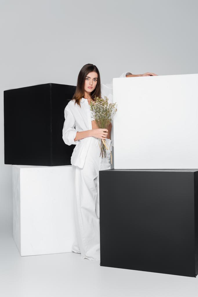 brunette woman with flowers standing near black and white cubes on grey background - Photo, Image