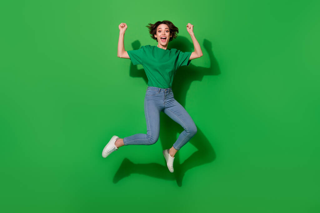 Ganzkörperporträt von entzückten zufriedenen Mädchen springen heben Fäuste schreien ja isoliert auf grünem Hintergrund. - Foto, Bild