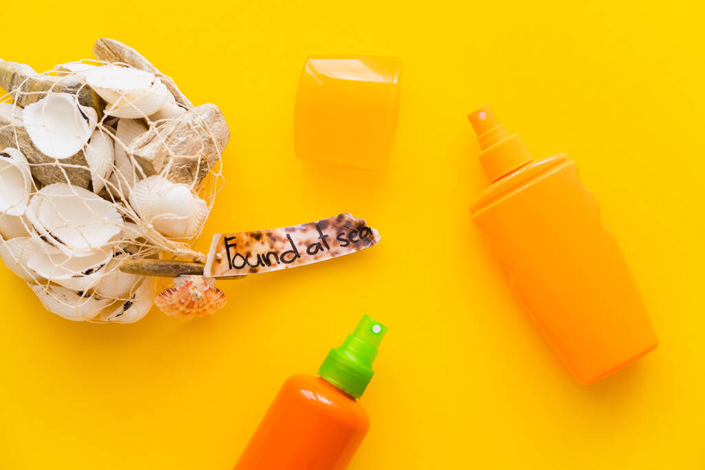 Draufsicht auf Muscheln mit gefundenen Schriftzügen in der Nähe von Sonnenschutzmitteln auf gelbem Hintergrund  - Foto, Bild