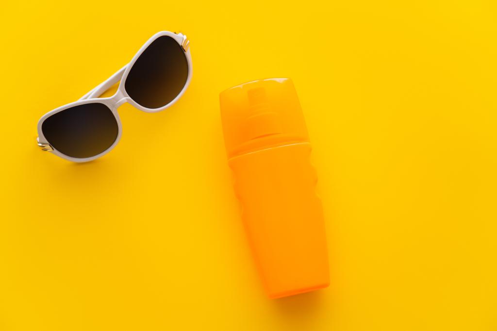 Vista superior de las gafas de sol cerca del protector solar sobre fondo amarillo  - Foto, Imagen