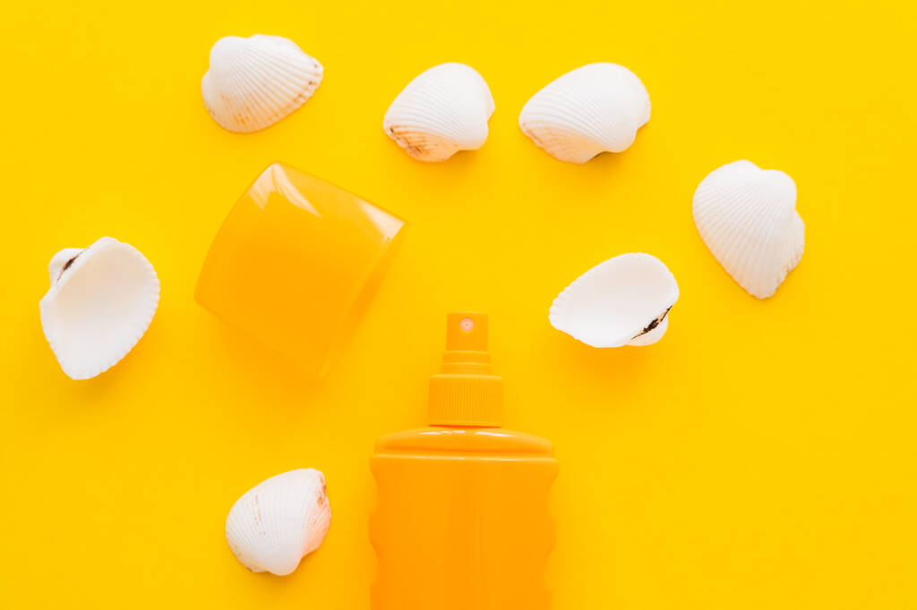 Top kilátás palack fényvédő közelében fehér kagylók sárga háttér  - Fotó, kép