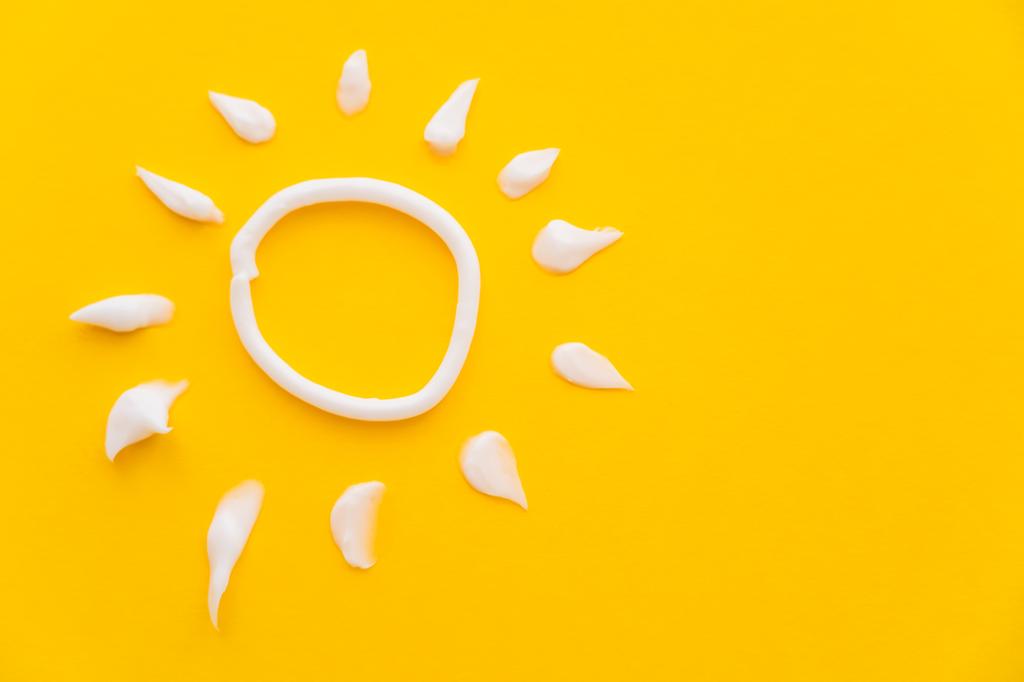 Верхний вид солнца знак от солнцезащитного крема на желтом фоне  - Фото, изображение