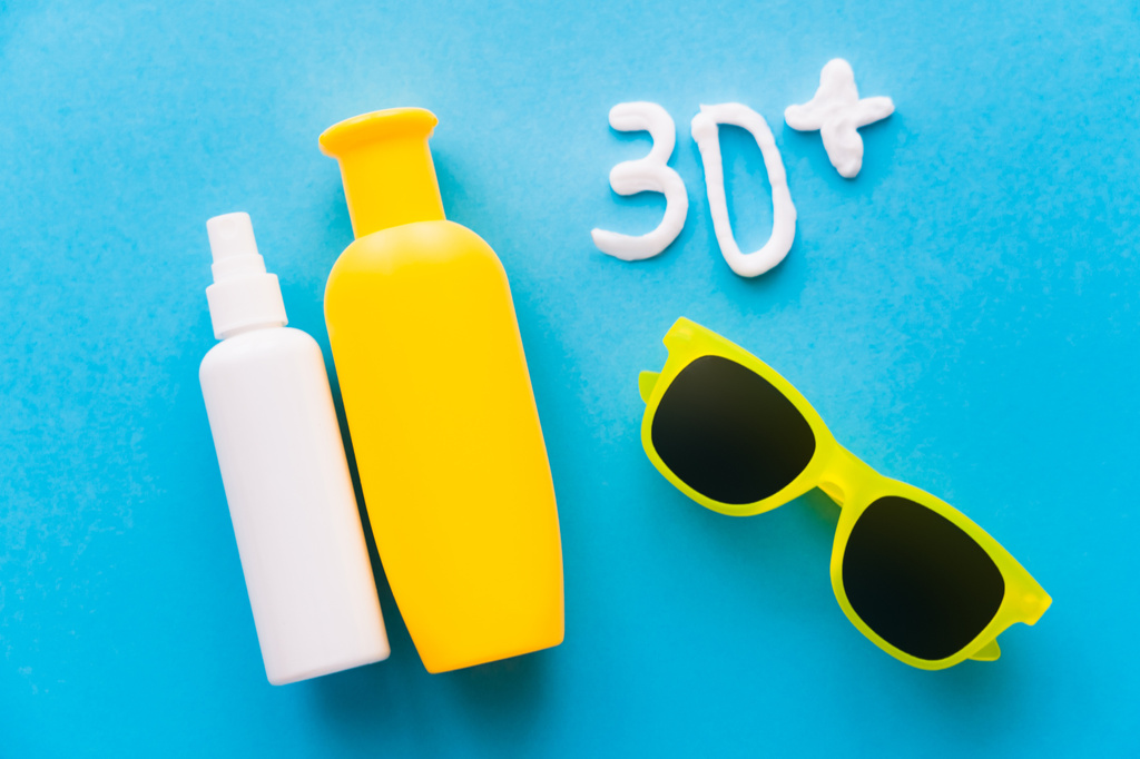 Sonnenschutzmittel in der Nähe von 30 + Schildern und Sonnenbrillen auf blauem Hintergrund  - Foto, Bild