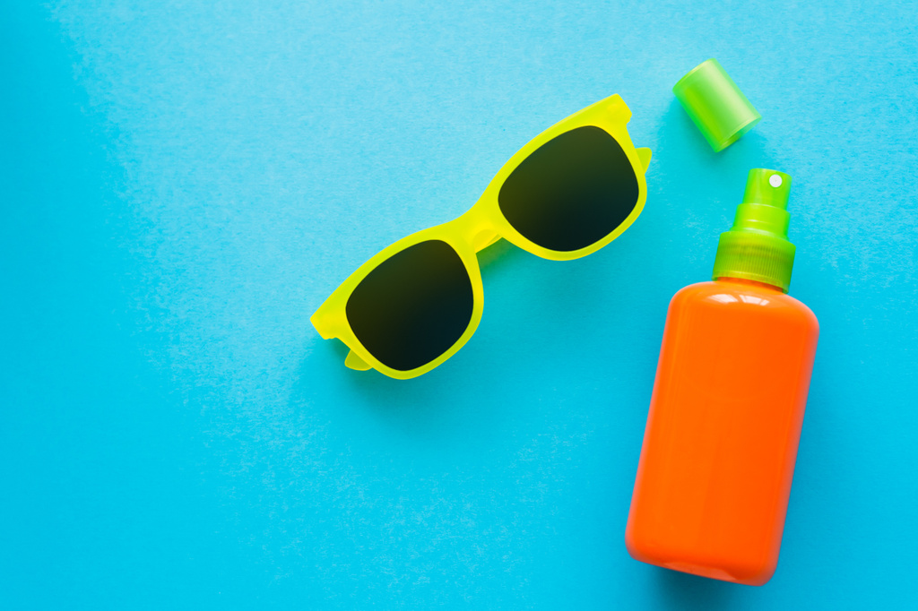 Vue du dessus des lunettes de soleil près de la bouteille de crème solaire sur fond bleu  - Photo, image