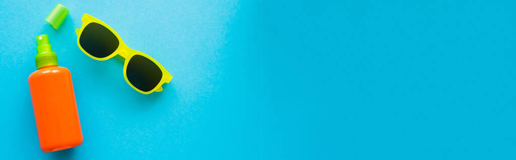 Верхний вид бутылки солнцезащитного крема и солнцезащитных очков на голубом фоне, баннер  - Фото, изображение