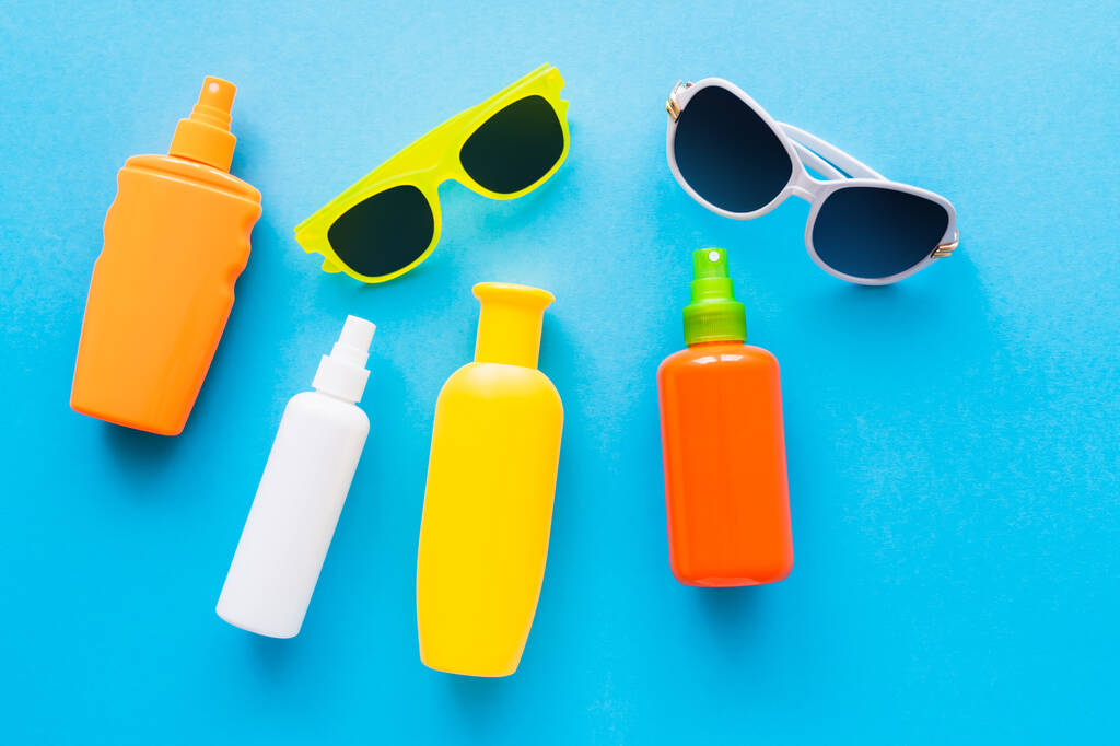 Верхний вид солнцезащитных очков и солнцезащитных кремов на синем фоне  - Фото, изображение