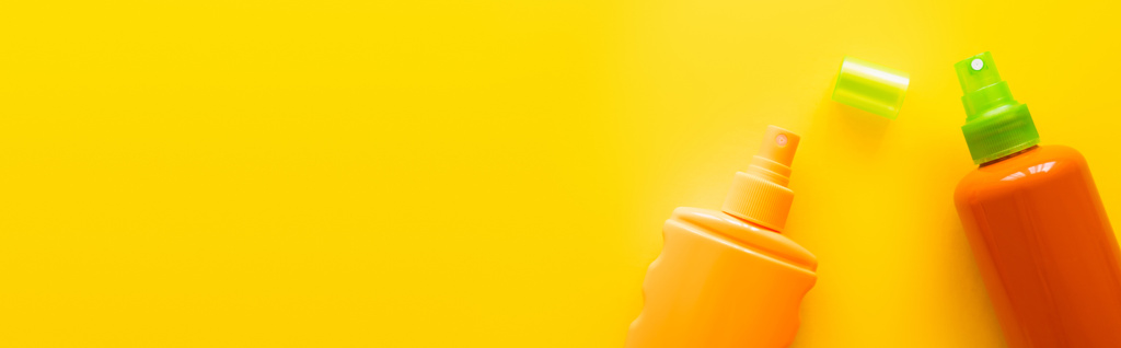 Bovenaanzicht van flessen zonnebrandmiddelen nabij dop op geel oppervlak, banner  - Foto, afbeelding