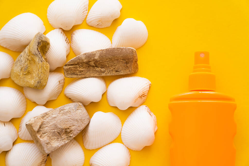 Top view of seashells and stones near sunblock on yellow background  - Photo, Image