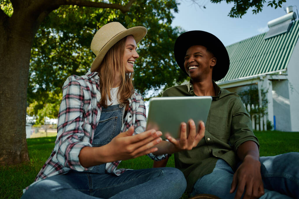 Przyjaciółki pracujące na farmie, patrzące na cyfrowe tablety, uśmiechające się do siebie. Wysokiej jakości zdjęcie - Zdjęcie, obraz