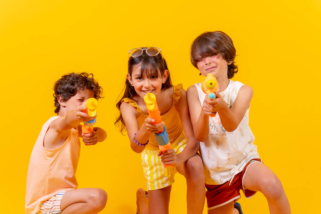 Παιδιά που διασκεδάζουν με νεροπίστολα στις καλοκαιρινές διακοπές, κίτρινο φόντο - Φωτογραφία, εικόνα