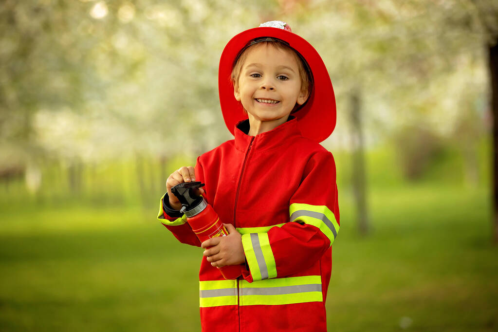 Little toddler child with fireman costume in park, pretending to be real fireman, playing on sunset - 写真・画像