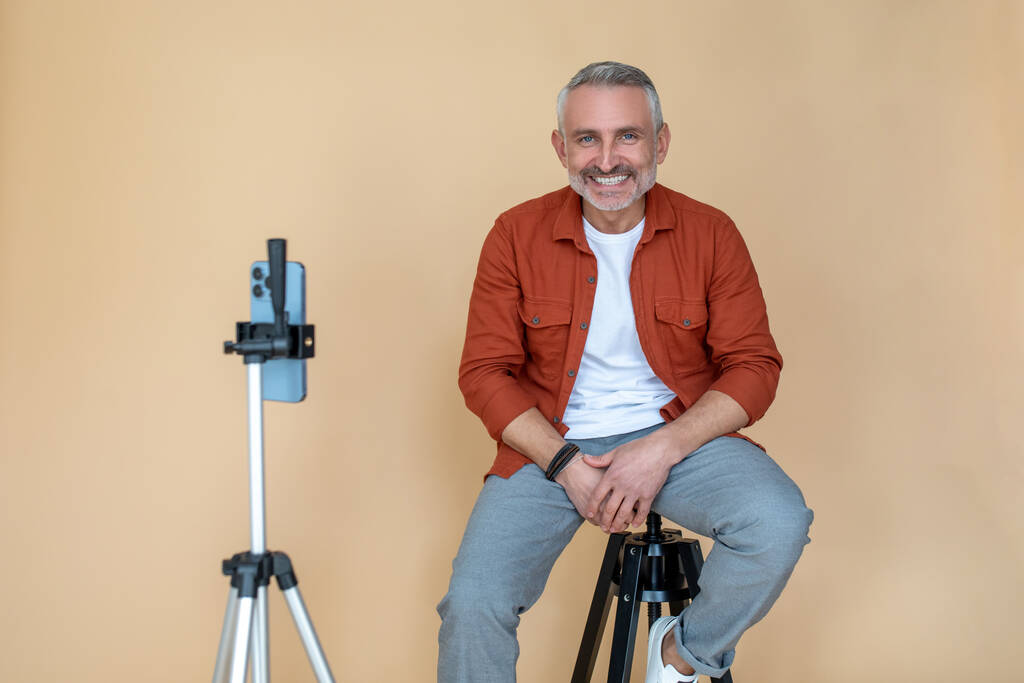 Selfie. A man in a red jacket sitting on a stool in a studio and making selfie - Photo, Image