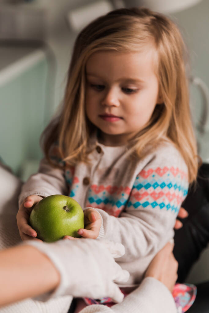 Mała dziewczynka trzymająca jabłko w rękach. Biuro stomatologiczne - Zdjęcie, obraz