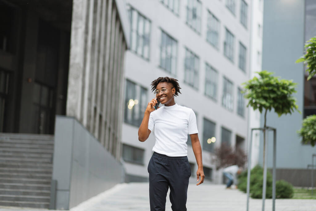 Foto van verbazingwekkende mooie Afro-Amerikaanse dame, tijd doorbrengen op straat na college, telefoon vasthouden tijdens een gesprek met beste vriend. - Foto, afbeelding