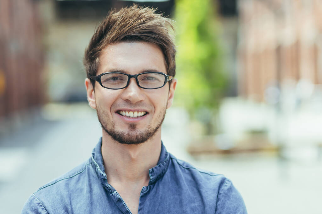 Detailní záběr portrét mladého muže s vousy na volné noze podnikatel v brýlích při pohledu na fotoaparátu s úsměvem - Fotografie, Obrázek
