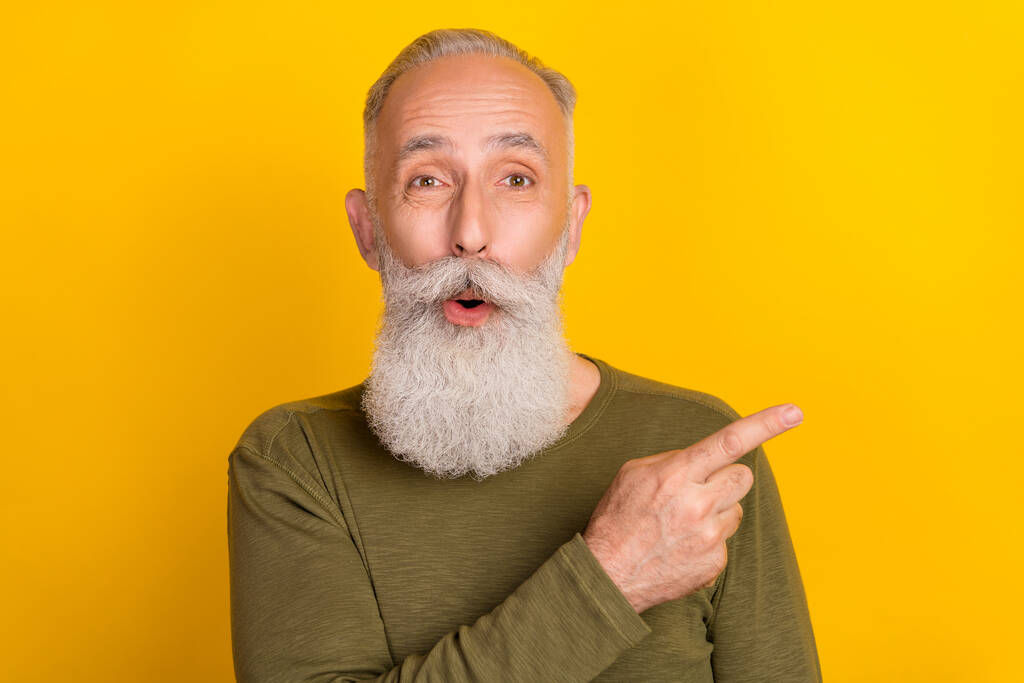 Foto di impressionato invecchiato bianco barba uomo punto vuoto spazio usura maglione verde isolato su sfondo di colore giallo. - Foto, immagini