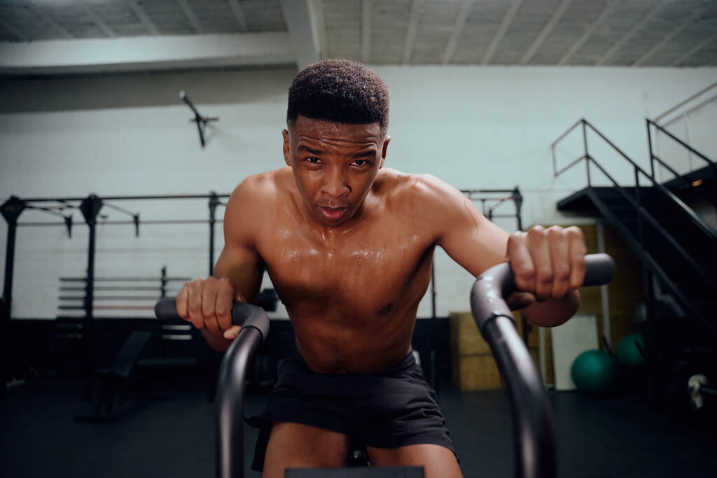 Afroamerykanin korzystający z orbitreka podczas treningu crossfit. Mężczyzna trener osobisty ćwiczenia intensywnie na siłowni. Wysokiej jakości zdjęcie - Zdjęcie, obraz