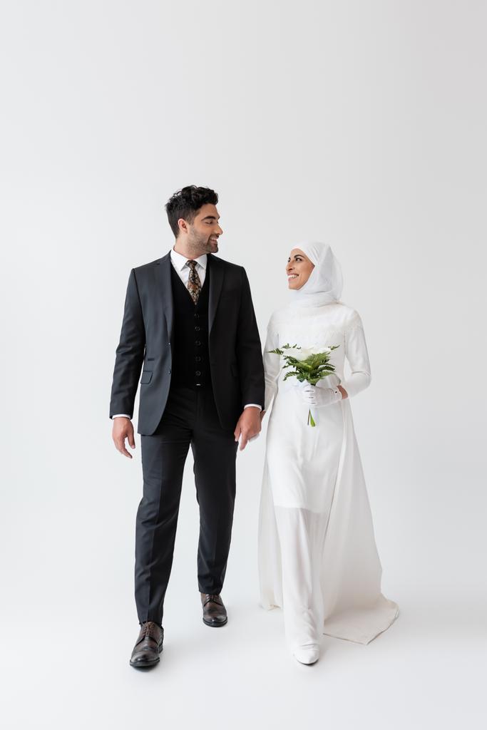 Muslimische Braut im Hochzeitskleid mit einem Strauß Calla-Lilie und einem glücklichen Bräutigam im Anzug auf grau - Foto, Bild