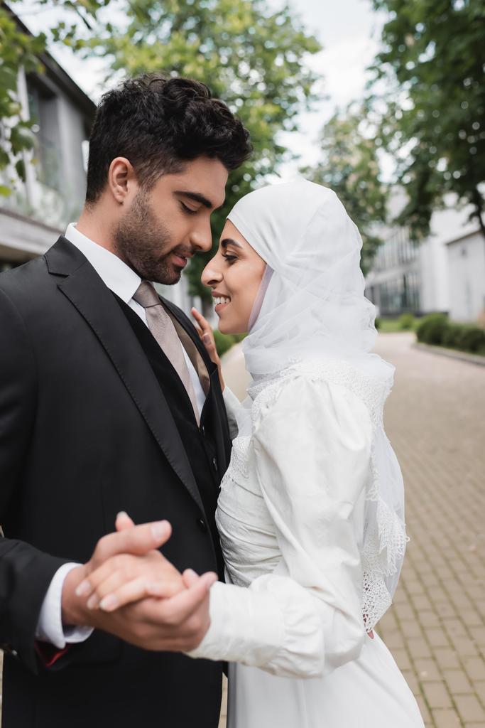 szczęśliwy muzułmanin panna młoda i pan młody z zamkniętymi oczami trzymając się za ręce - Zdjęcie, obraz