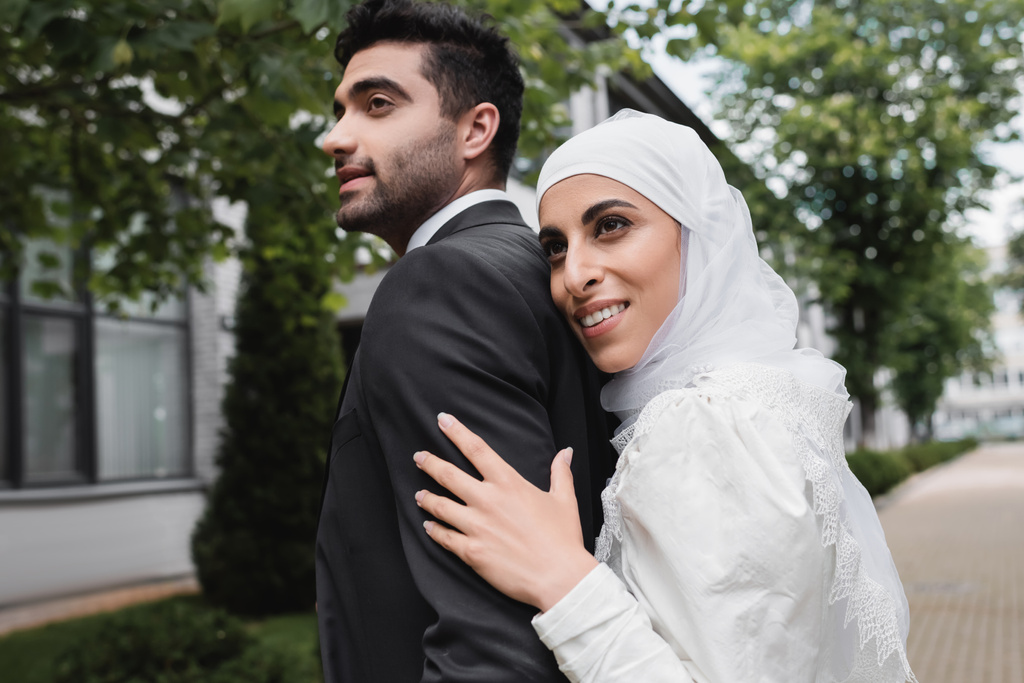 幸せなイスラム教徒の花嫁でヒジャーブとウェディングドレス抱擁新郎  - 写真・画像