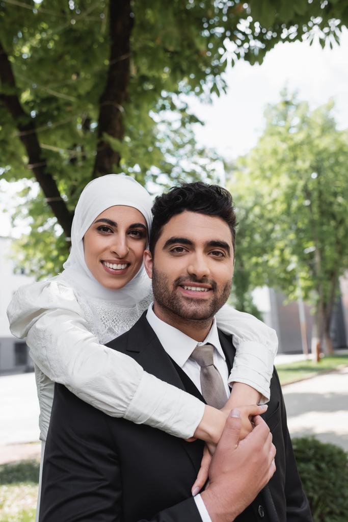 sposa felice in hijab abbracciando allegro sposo musulmano in abito  - Foto, immagini