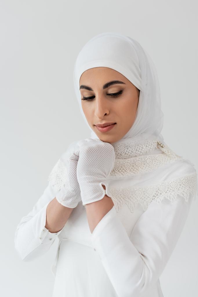 πορτρέτο της μουσουλμανικής νύφης σε λευκό χιτζάμπ και νυφικό κοιτάζοντας προς τα κάτω απομονώνονται σε γκρι  - Φωτογραφία, εικόνα