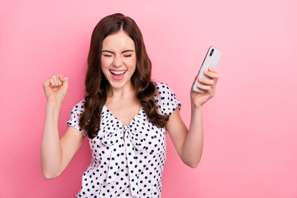 Фото фанки восторженный девушка поднять кулаки в победу победу в социальных сетях телефон раздачи изолированы на розовом фоне. - Фото, изображение